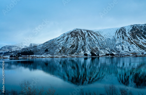 Perfect mountain reflection in calm fjord water during winter in Lofoten Islands, Norway. Scenic Arctic landscape with snow covered peaks and still sea. Beautiful Nordic nature background for Scandina