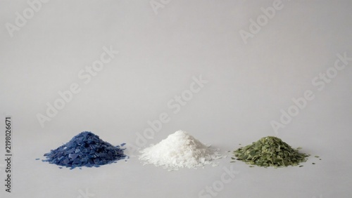 Heaps of washed blue white and green plastic regrind flakes on grey studio paper