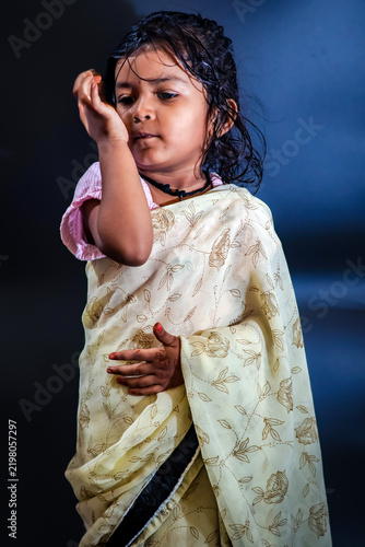 Obraz na plátně Cute little girl holding hand near face with coy expression in traditional saree