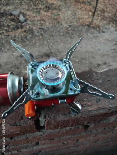 Portable camping gas stove with blue flame burning on a brick surface outdoors