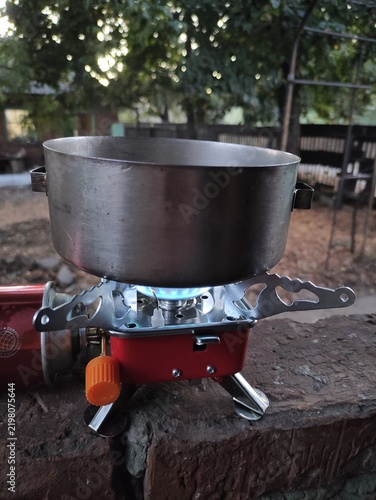Portable camping gas stove with metal pot heating on a brick wall outdoors