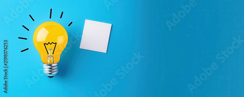 A bright yellow light bulb with black rays beside a blank white square note on a vibrant blue background.