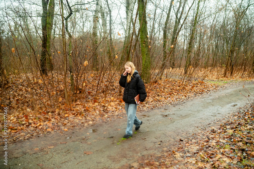 Fototapeta premium Young Woman Walking Along a Forest Path Talking on Smartphone During Autumn