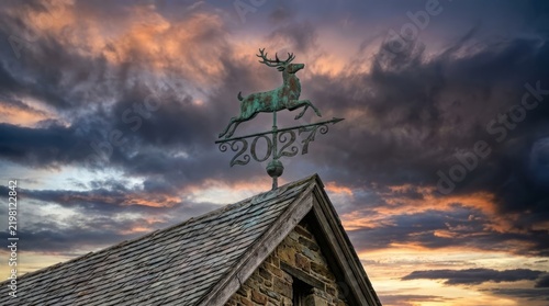 Metal deer weathervane showing the year 2027 against a dramatic sunset sky