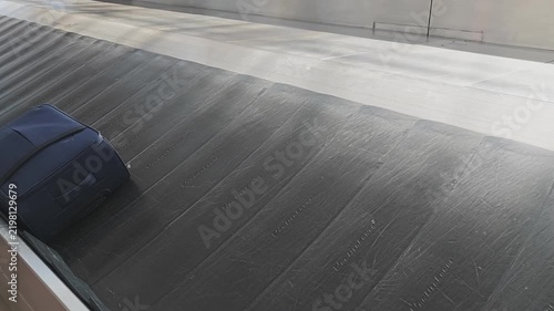Empty airport baggage claim carousel in motion. A single blue suitcase with wheels appears and moves along the conveyor belt for pickup