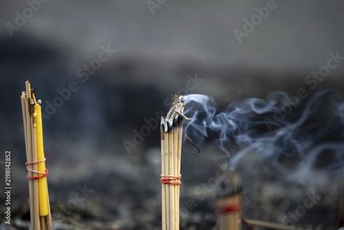 Fine smoke rises between the upright incense sticks and forms soft, swirling lines in the warm air. The bundles are carefully tied and depict a serene scene of traditional offerings such as those found in many temples and shrines, Wat Yai Chai Mongkon, Ayutthaya, Thailand