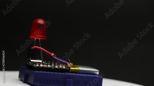 Breadboard with small microcontroller powered by lithium polymer battery, red LED blinking on and off as the whole setup rotates