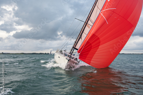 Obraz na plátně Segelyacht mit leuchtend rotem Gennaker spaltet dynamisch das raue Meer unter be