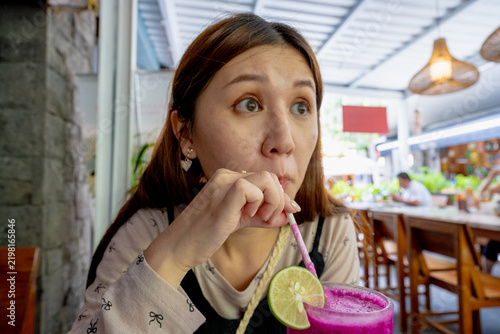 BALI, INDONESIA – OCTOBER 20, 2024: Young woman drinking fresh pitaya dragon fruit smoothie with a straw in Ubud cafe.