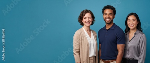 Three business colleagues, two women and one man, smiling together in front of teal background. Multiethnic corporate coworkers standing proudly representing workforce diversity and unity.