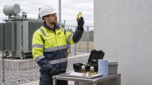 Technician inspecting transformer oil sample at substation
