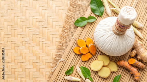 Herbal compress ball with turmeric root and ginger on woven bamboo mat.