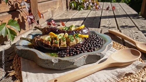 Roasted eggplant boats filled with herbed golden vegetables beside black lentils, lemon and parsley, served on handmade pottery over a weathered porch table in crisp afternoon sunlight at harvest