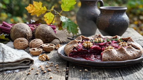 Beet galette with walnuts, red onion and thyme on a dark ceramic plate, surrounded by whole beets, cracked shells and flour on a weathered table in mellow garden light and rich harvest color