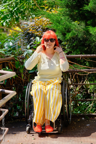 A model in a wheelchair with bright red hair is posing.