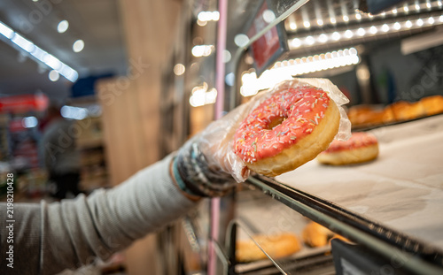 Woman's hand selects a donut with pink icing and sprinkles in a supermarket during a shopping trip