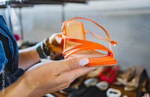 Cuadro en lienzo Close-up of woman's hands holding bright orange strappy sandal while browsing se