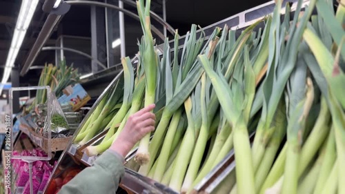 Shopper Selecting Fresh Green Leeks in Supermarket Aisle