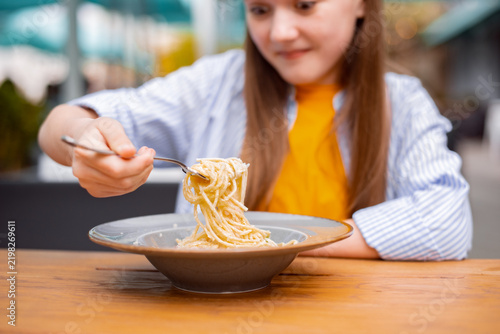 Konstfotografi Cute teen girl enjoying freshly cooked spaghetti carbonara outdoors