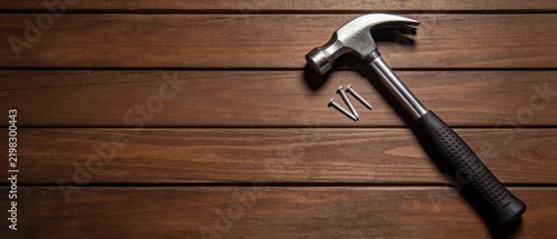 A claw hammer and nails resting on a dark wooden surface