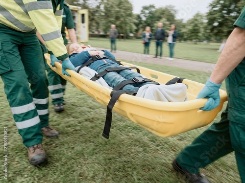 Emergency paramedics transport patient on stretcher through park during medical rescue
