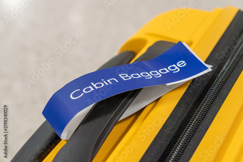 Bright yellow suitcase featuring a blue cabin baggage tag, representing travel, air transport, and packing for a journey