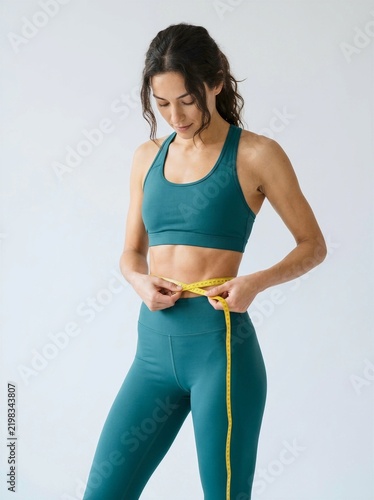 Woman in athletic wear measures waist with tape measure during fitness workout