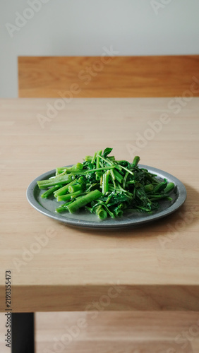 Stir fried water spinach on a plate by a bright window