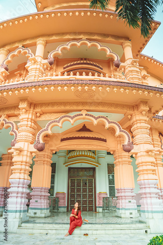 Portrait of a young Indian woman in traditional dress standing at a Hindu temple complex in South Delhi, India, with marble and carved stone architecture in the background.
