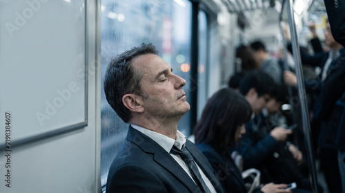 通勤電車の車内で目を閉じて居眠りをする疲れた外国人ビジネスマン