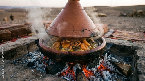 Traditional Moroccan tajine dish cooking with tender meat and dried apricots over glowing hot desert campfire coals at sunset hour