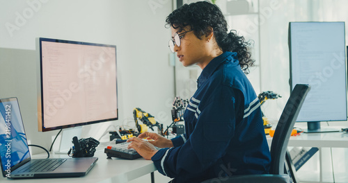 Obraz na płótnie Young African American female robotics engineer coding AI software for robotic arm in laboratory