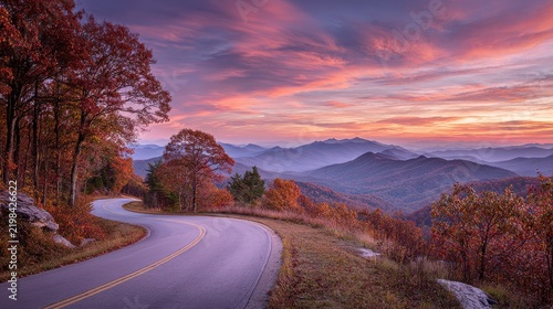 Winding road curves through colorful autumn mountains under a vibrant sunset sky. Scenic travel background.