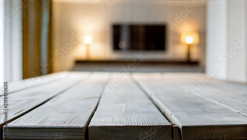 an empty weathered wooden tabletop with a prominent natural grain and gray-toned finish in front of blurred warm lighted interior.