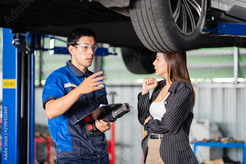 Fotografie A customer in a service garage hears a technician explain EV battery findings under the lift with clipboard and work light