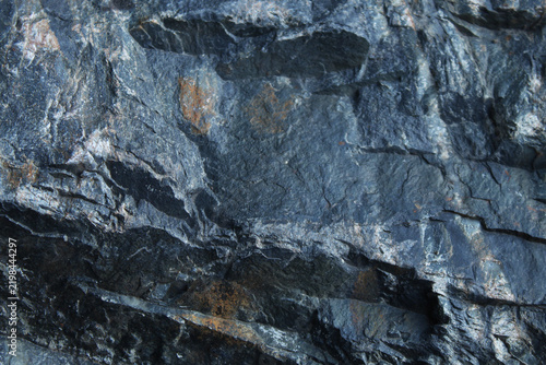 Rugged dark grey rock face with sharp faceted texture and deep crevices
