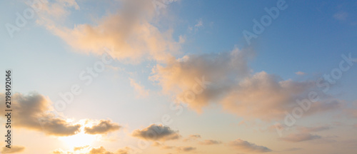 Panoramic Golden Hour Sky with Soft Clouds at Sunset,A wide panoramic photograph of a soft sunset sky featuring golden-lit clouds against a blue and pale yellow gradient backdrop. Ideal for web header