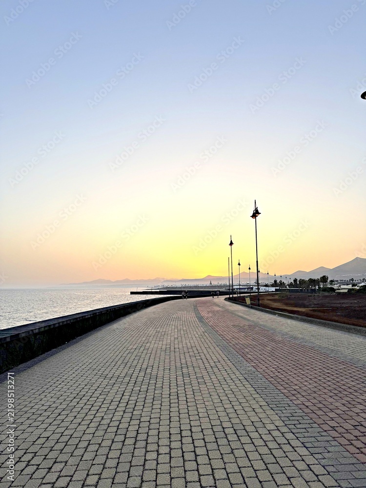 Fototapeta premium Seaside promenade at sunset with cobblestone path and sea