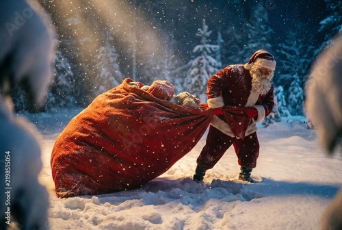 Santa Claus dragging a massive bag of gifts through winter snow