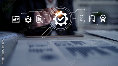 A businessman interacts with a tablet, using a magnifying glass to explore digital icons that symbolize quality control and business analysis in a modern office setting. Nascent