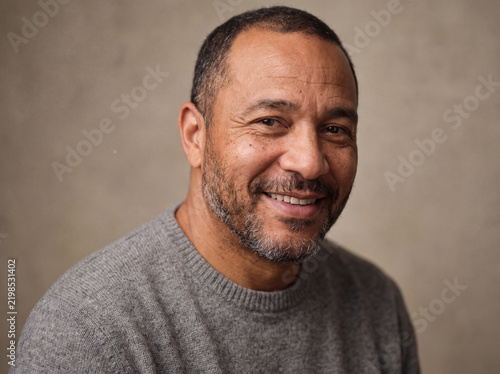 Genuine portrait of a middle-aged man with natural skin texture and short beard smiling warmly against a neutral studio background