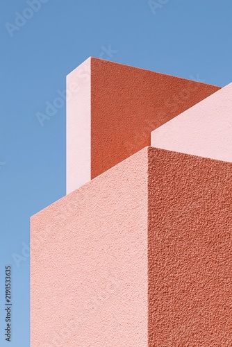 Minimal geometric architecture with coral pink textured walls against a clear blue sky
