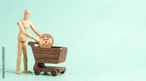 Marketing team KPI and employee performance evaluation concept with wooden mannequin putting top pick badge in shopping cart with copy space for business growth presentation banner