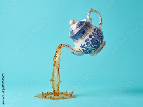 Porcelain teapot pouring tea in midair on turquoise background