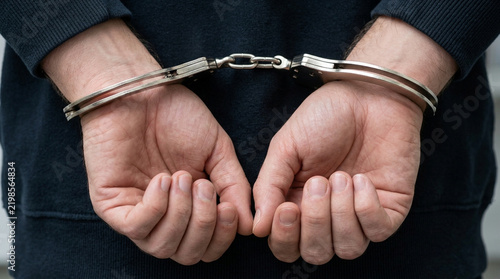 Person's hands cuffed behind back, close-up on handcuffs and wrists.
