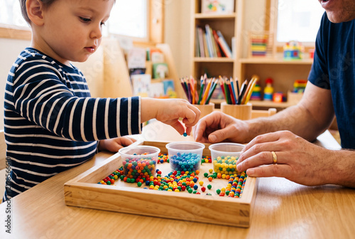 Child Development and Fine Motor Skills Activity with Father or Therapist Sorting Colorful Beads in Early Learning Classroom