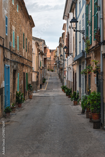 Narrow street with traditional stone houses and colorful shutters in Arta, Mallorca, Spain