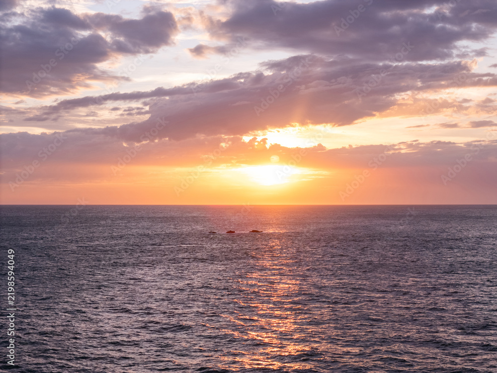 Obraz premium Sunset over the ocean with clouds and waves in the background
