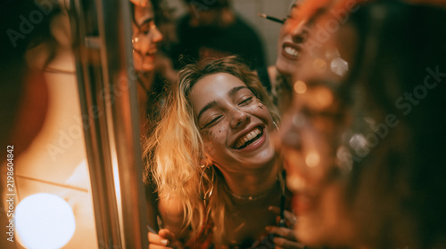 A Night of Revelry: A young woman with a radiant smile shares a moment of pure joy and laughter with friends at a vibrant party, illuminated by warm, festive lights.