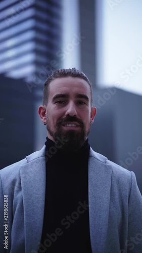 Portrait of a confident caucasian businessman looking at the camera smiling, standing in front of financial district. Vertical headshot footage with copy space.